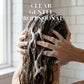 Person washing hair with soapy hands in a bathroom setting, with text 'Clear. Gentle. Professional.'